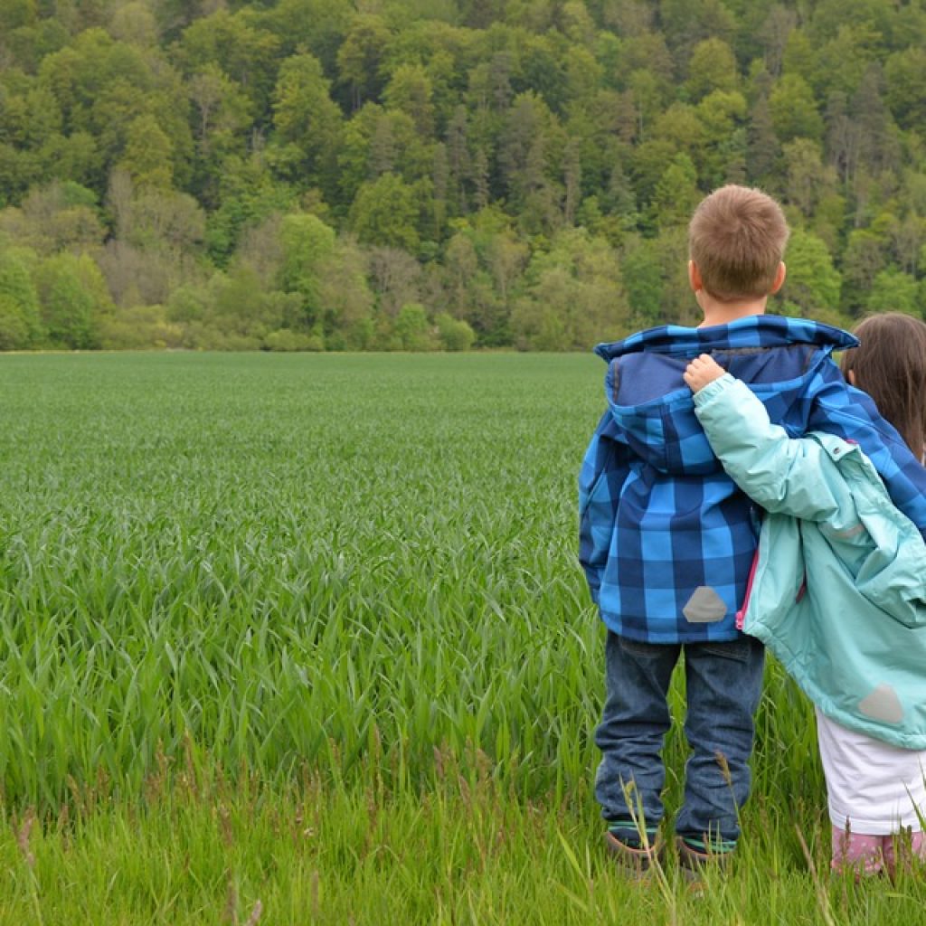 Kinder spazieren im Gras und tragen lange Kleinung, um sich vor Zecken zu schützen