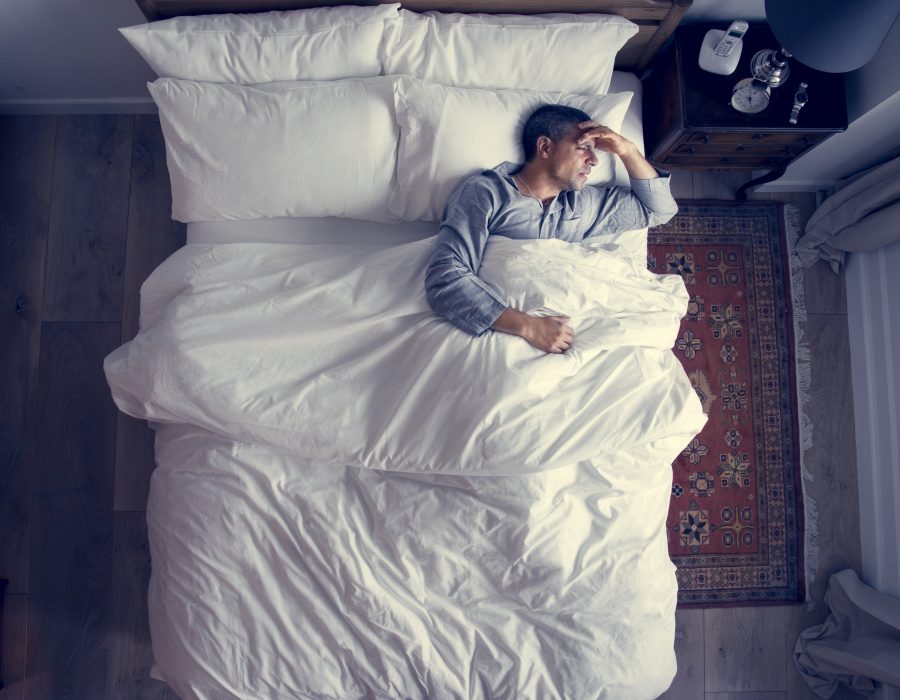 Mann im Bett wacht auf, weil er an Kopfschmerzen und Migräne leidet